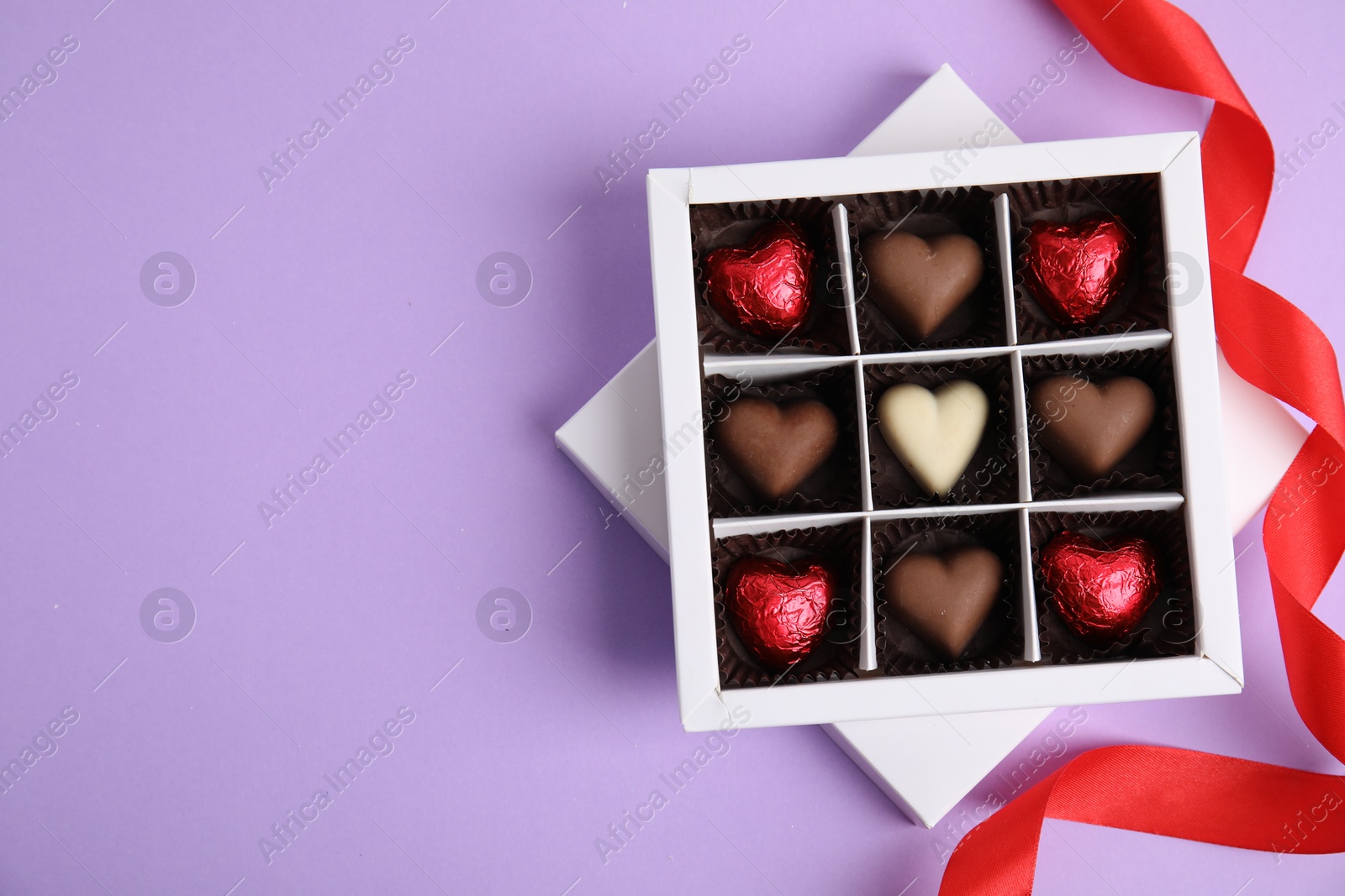 Photo of Tasty heart shaped chocolate candies on violet background, flat lay with space for text. Happy Valentine's day