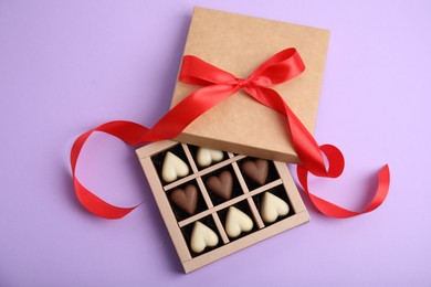 Photo of Tasty heart shaped chocolate candies on violet background, flat lay. Happy Valentine's day