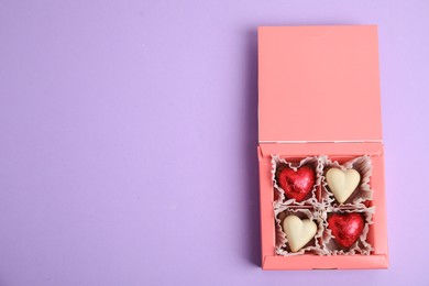 Photo of Tasty heart shaped chocolate candies on violet background, top view with space for text. Happy Valentine's day