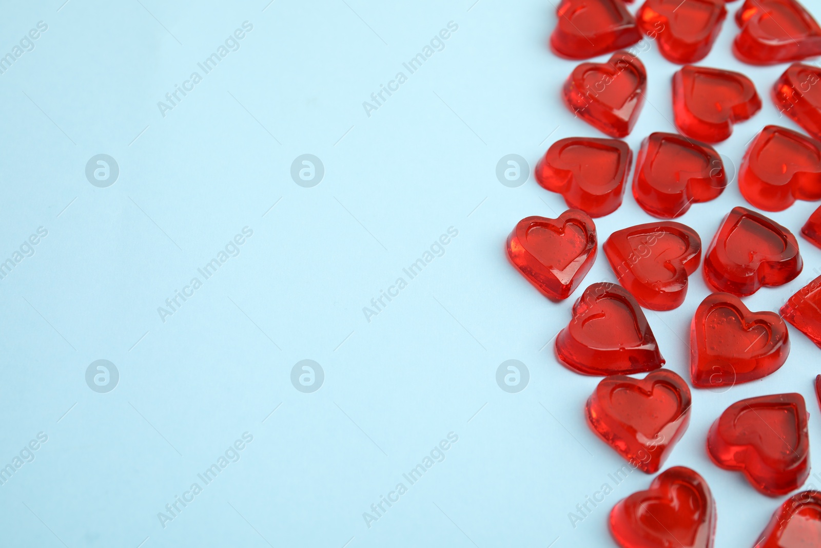 Photo of Sweet heart shaped jelly candies on light blue background, flat lay. Space for text