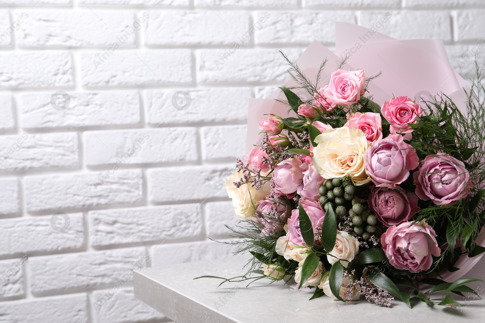 Photo of Beautiful bouquet with roses on light table near white brick wall. Space for text