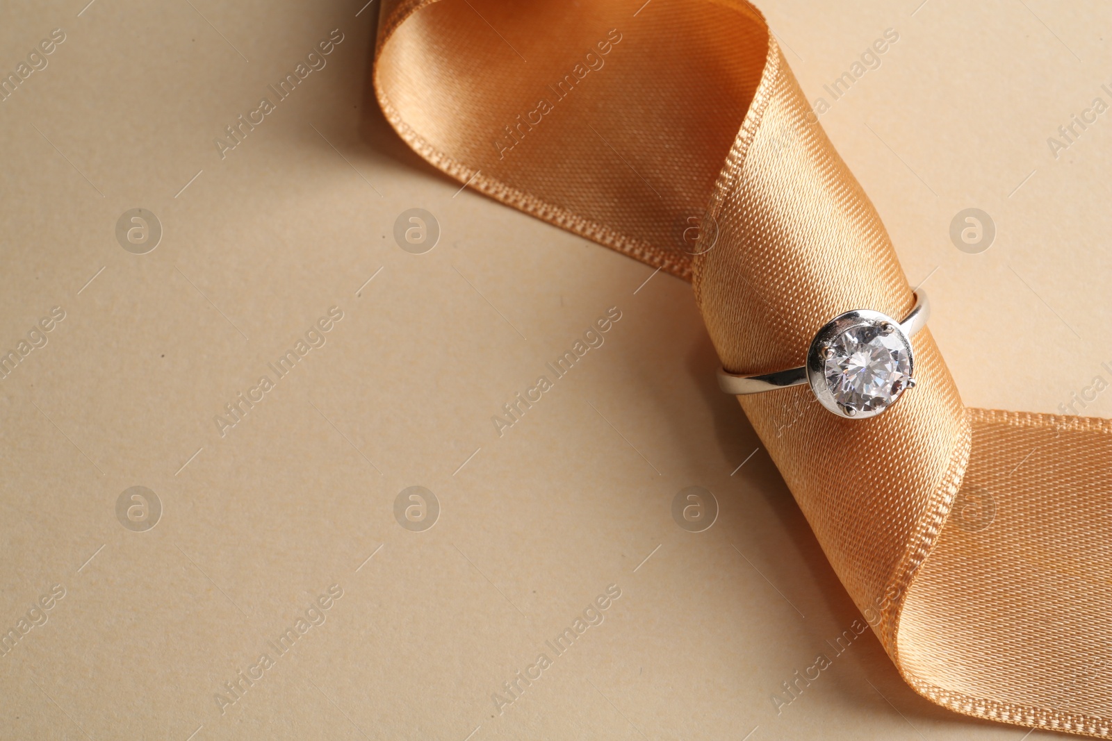 Photo of Beautiful luxury engagement ring with gemstone and ribbon on beige background, closeup. Space for text