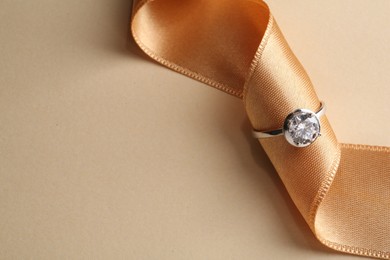 Photo of Beautiful luxury engagement ring with gemstone and ribbon on beige background, closeup. Space for text