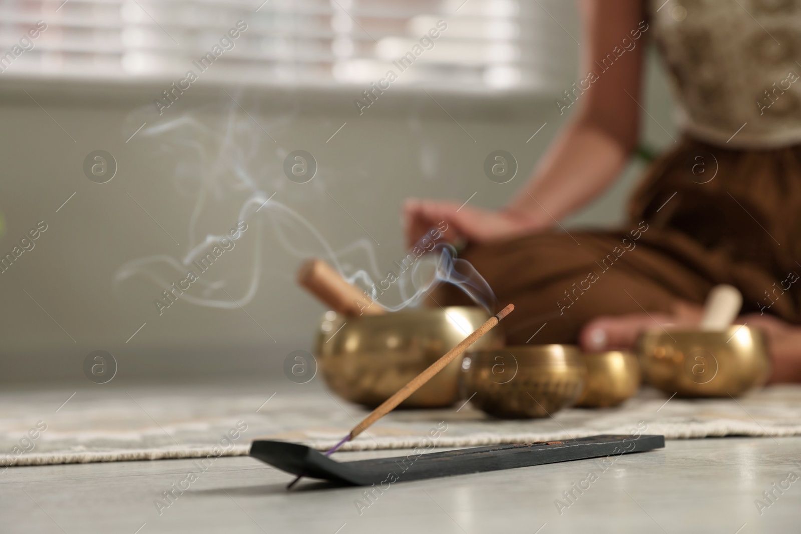 Photo of Incense stick smoldering in holder on floor indoors, selective focus