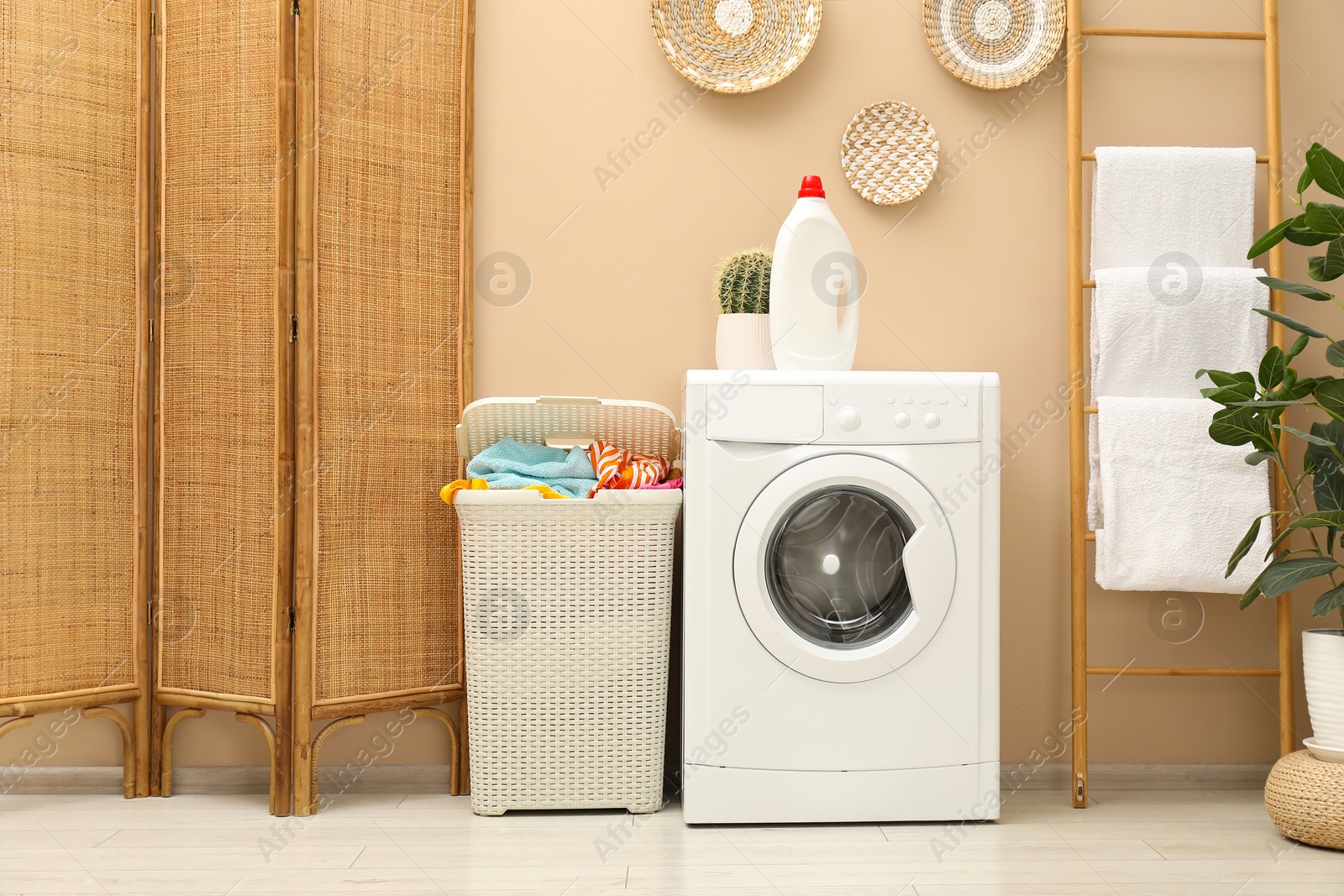 Photo of Wicker basket full of laundry, washing machine and detergent in bathroom