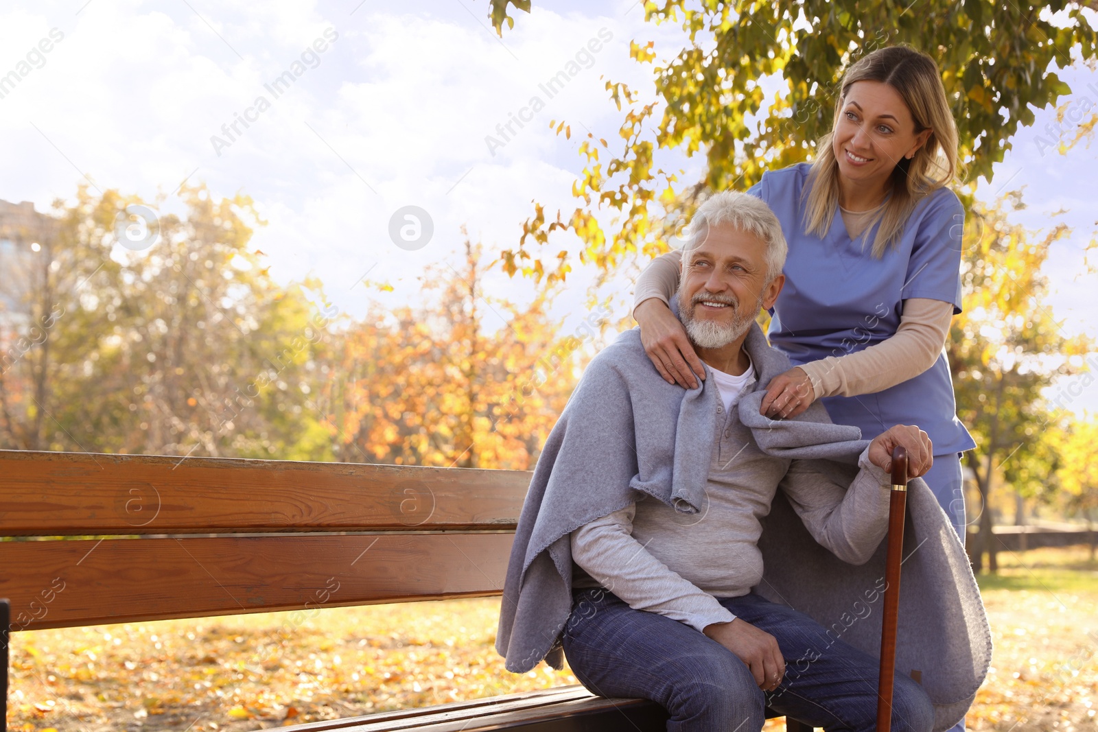 Photo of Caregiver assisting senior man on wooden bench in park, space for text. Home health care service