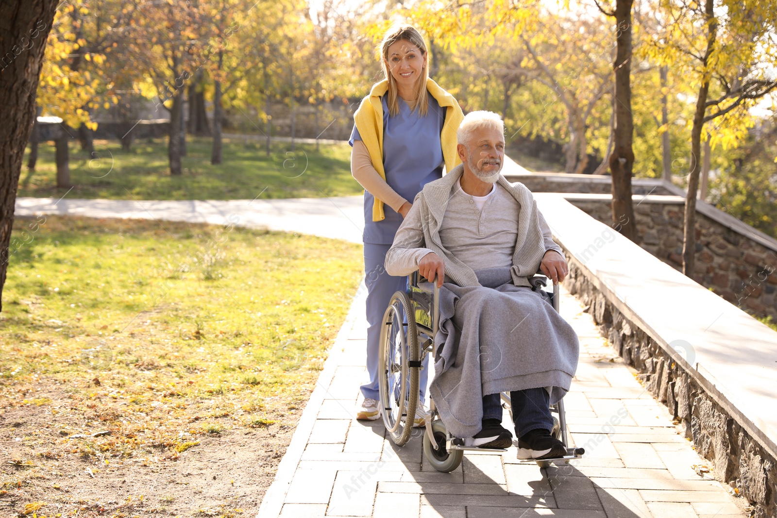 Photo of Caregiver assisting senior man on wheelchair in park, space for text. Home health care service