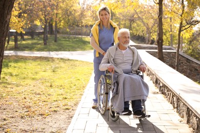 Caregiver assisting senior man on wheelchair in park, space for text. Home health care service