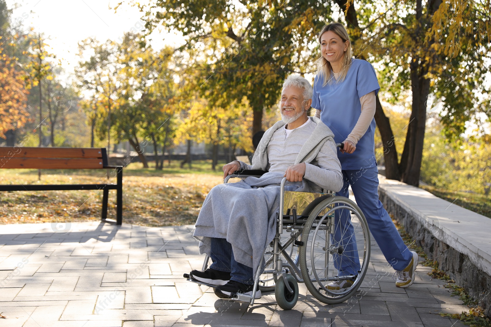 Photo of Caregiver assisting senior man on wheelchair in park, space for text. Home health care service