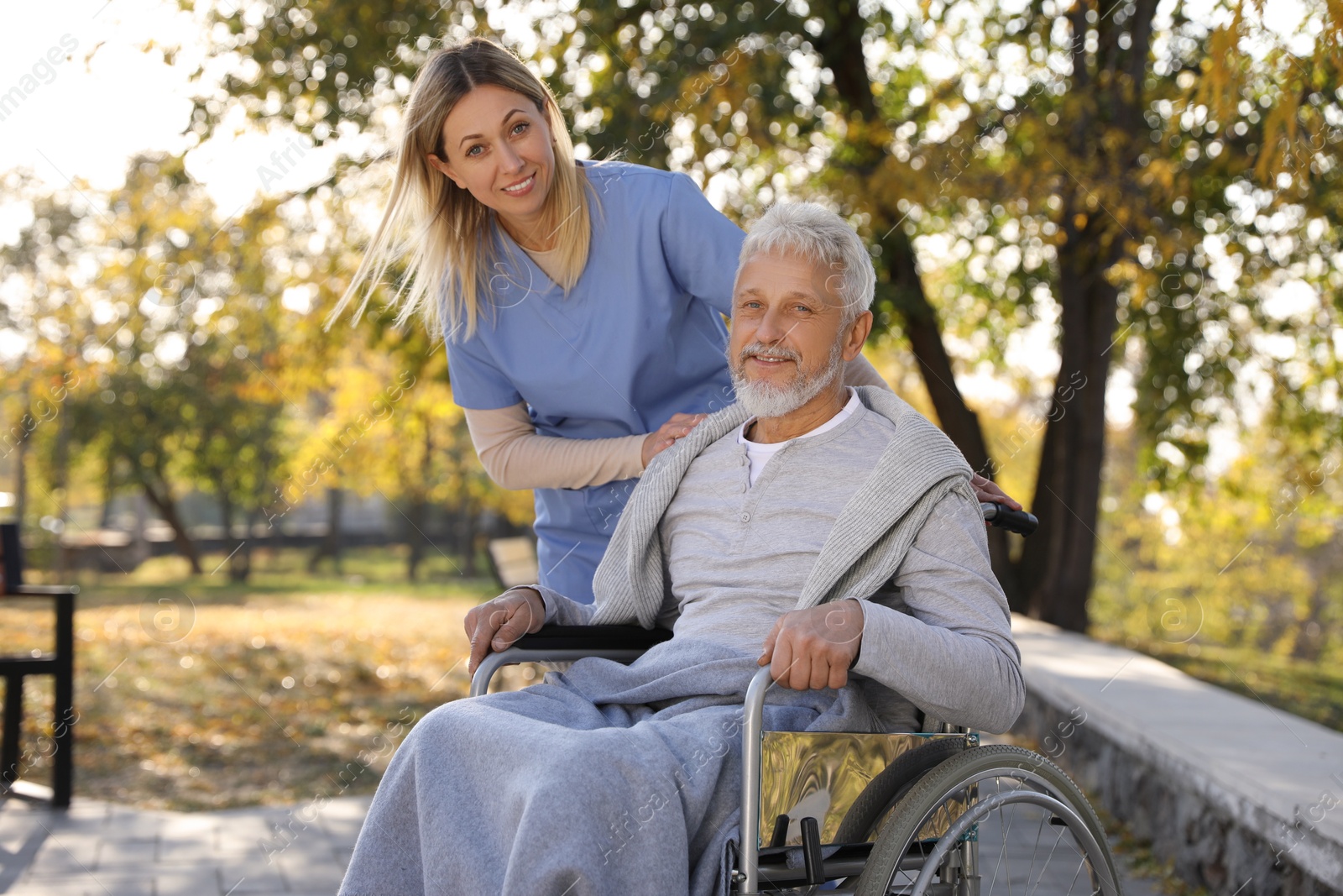 Photo of Caregiver assisting senior man on wheelchair in park. Home health care service