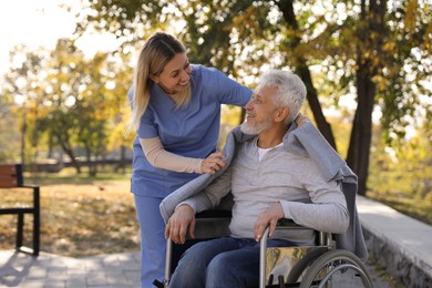 Photo of Caregiver assisting senior man on wheelchair in park. Home health care service