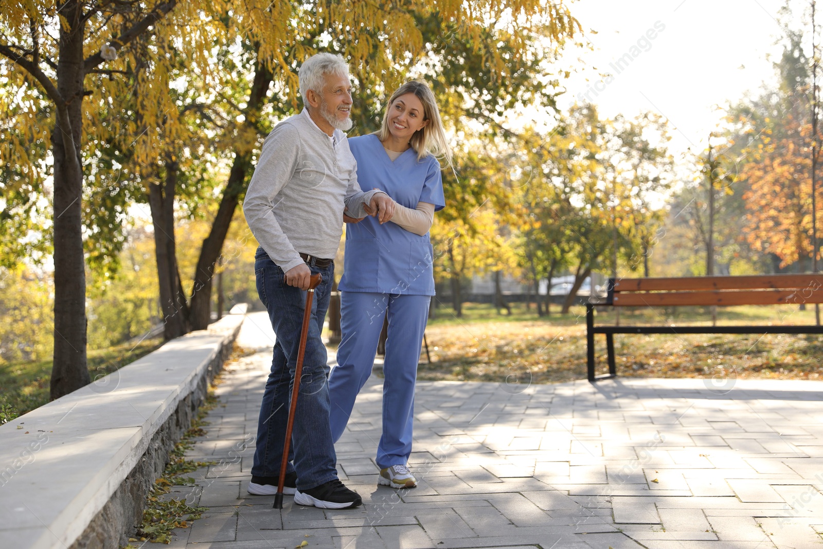 Photo of Caregiver assisting senior man in park, space for text. Home health care service