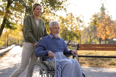 Caregiver assisting senior man on wheelchair in park, space for text. Home health care service