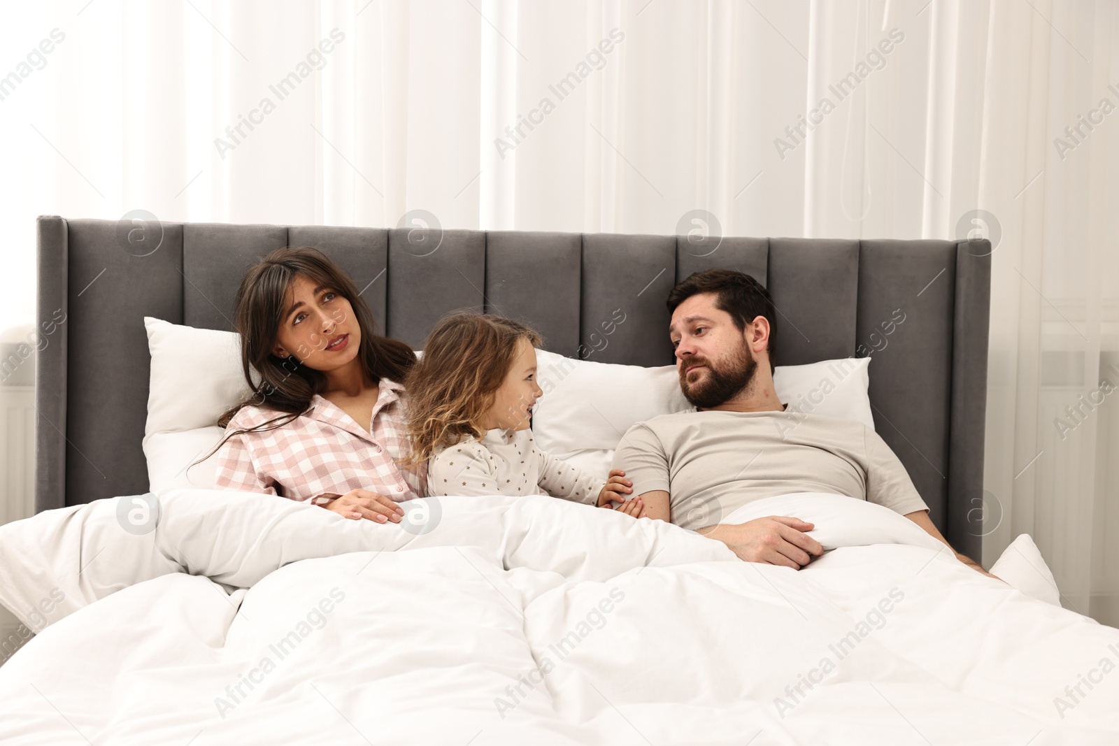 Photo of Happy playful daughter with her overwhelmed parents in bed at home