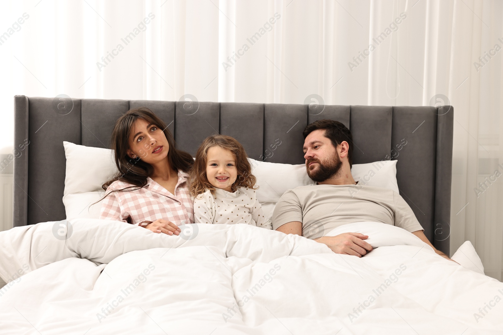 Photo of Happy playful daughter with her overwhelmed parents in bed at home