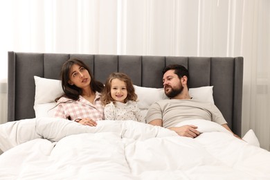 Happy playful daughter with her overwhelmed parents in bed at home