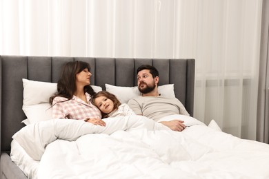 Photo of Playful daughter with her overwhelmed parents in bed at home