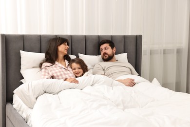 Photo of Happy playful daughter with her overwhelmed parents in bed at home