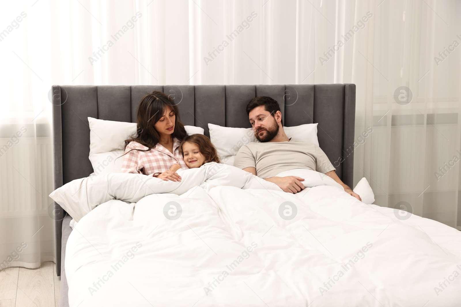 Photo of Playful daughter with her overwhelmed parents in bed at home