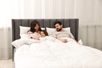 Playful daughter with her overwhelmed parents in bed at home