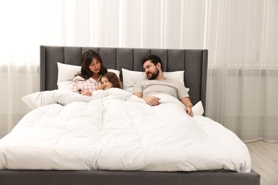 Playful daughter with her overwhelmed parents in bed at home