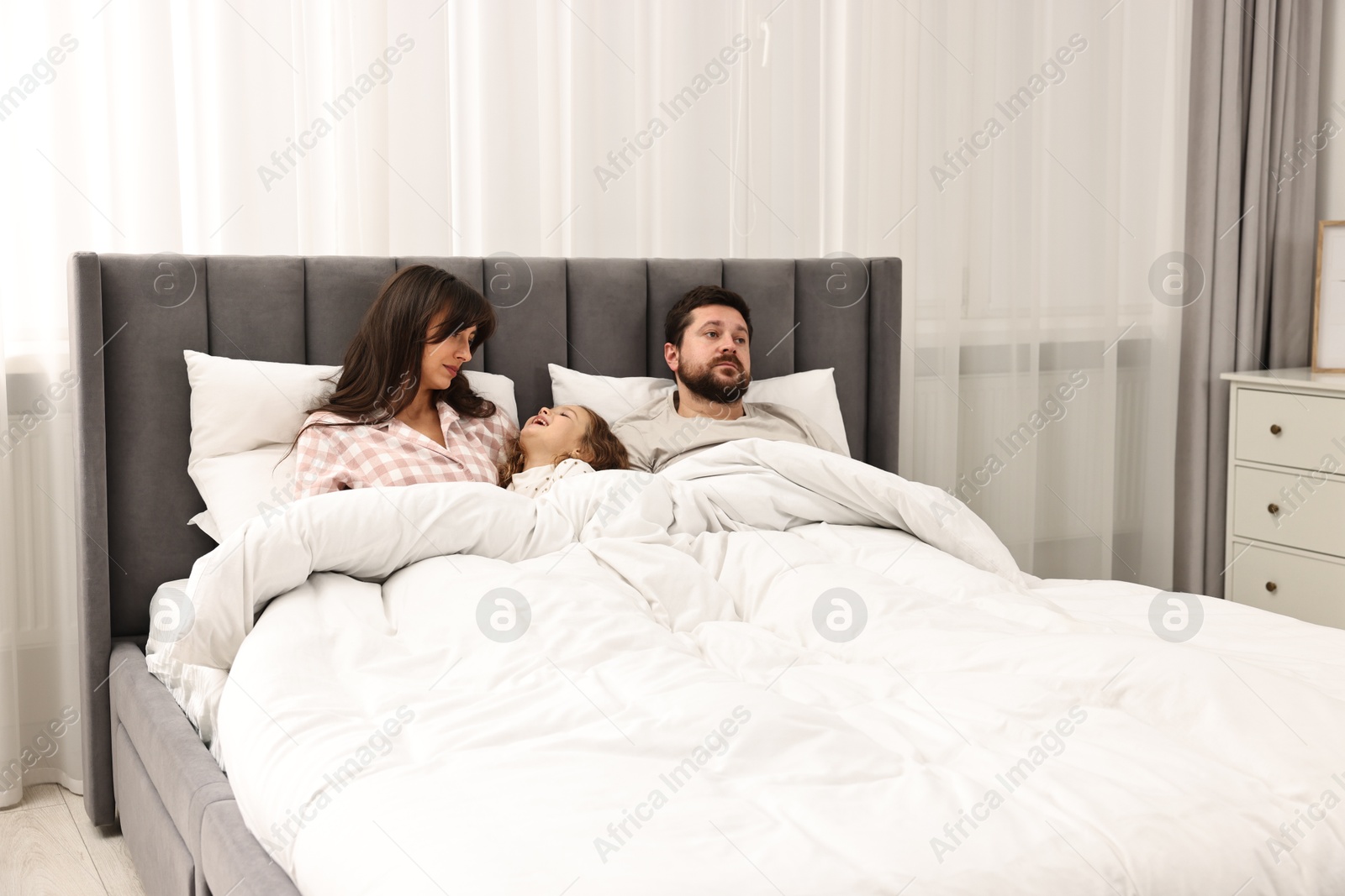 Photo of Happy playful daughter with her overwhelmed parents in bed at home