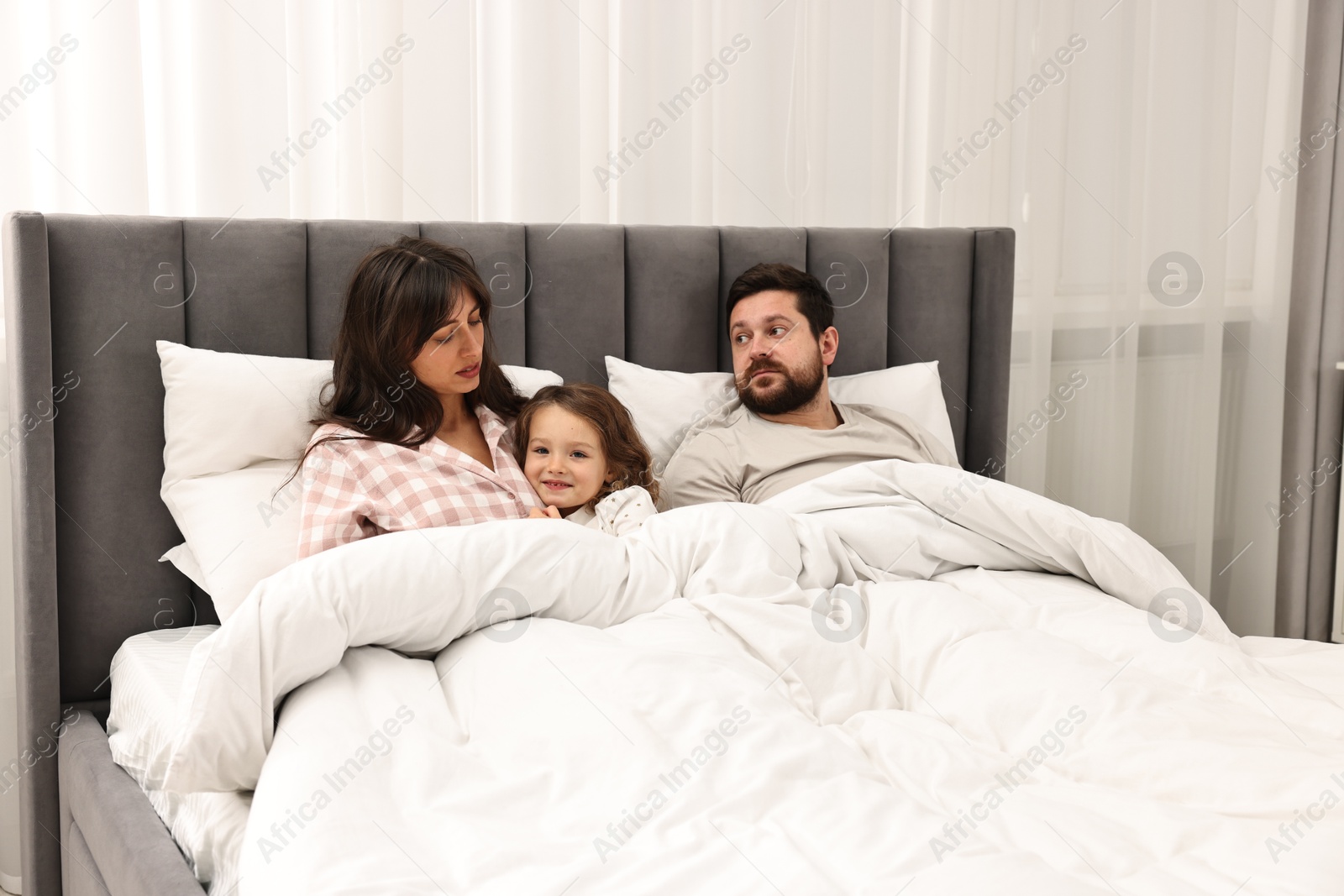 Photo of Happy playful daughter with her overwhelmed parents in bed at home