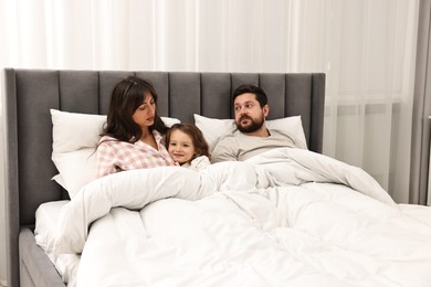 Happy playful daughter with her overwhelmed parents in bed at home