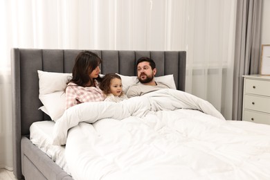 Photo of Little daughter with her overwhelmed parents in bed at home