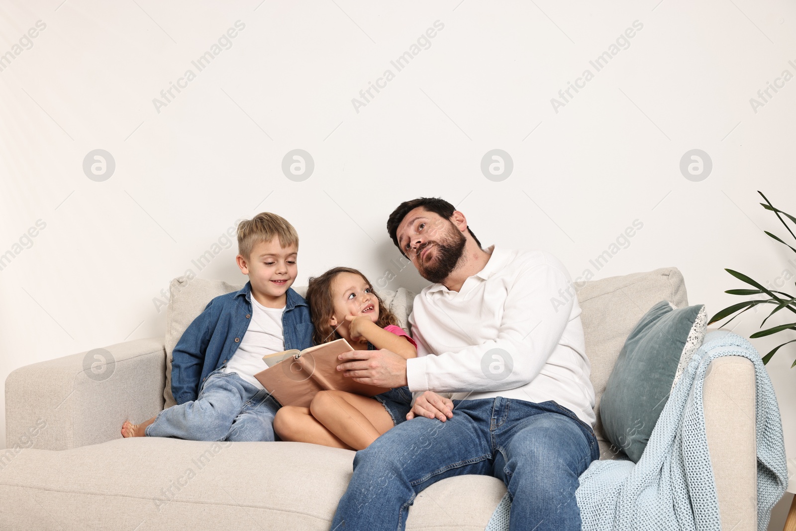 Photo of Overwhelmed father and his happy children on sofa at home