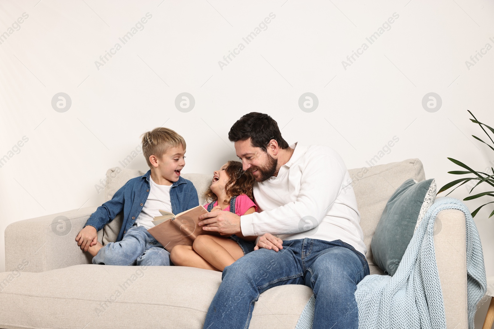 Photo of Happy father and his children reading book on sofa at home