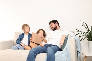 Overwhelmed father and his children reading book on sofa at home