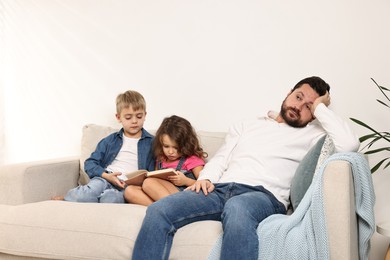 Photo of Overwhelmed father and his hyperactive children on sofa at home