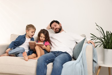 Photo of Overwhelmed father and his hyperactive children on sofa at home