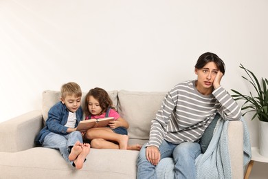 Overwhelmed mother and her naughty children with book on sofa at home