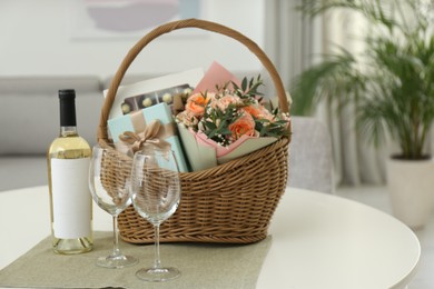 Photo of Wicker basket with gifts near bottle of wine and glasses on table indoors