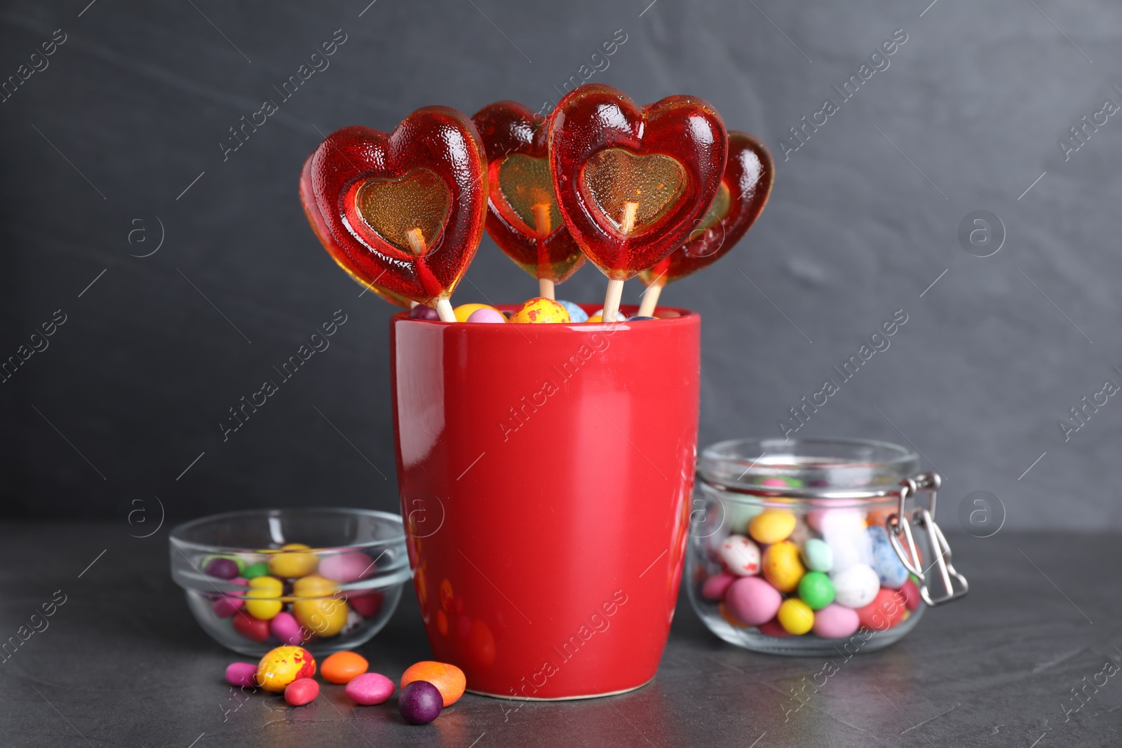 Photo of Delicious heart shaped lollipops and dragees on black table