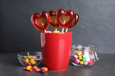 Photo of Delicious heart shaped lollipops and dragees on black table