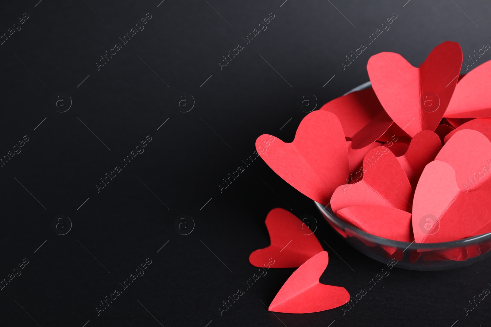 Photo of Red paper hearts in bowl on black background. Space for text