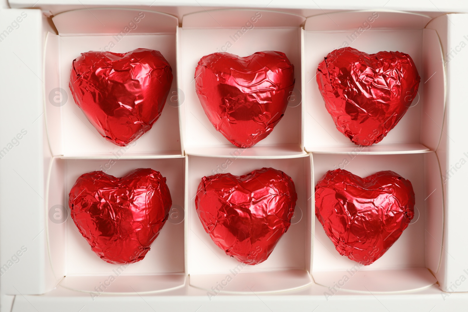 Photo of Tasty chocolate heart shaped candies in white box, top view