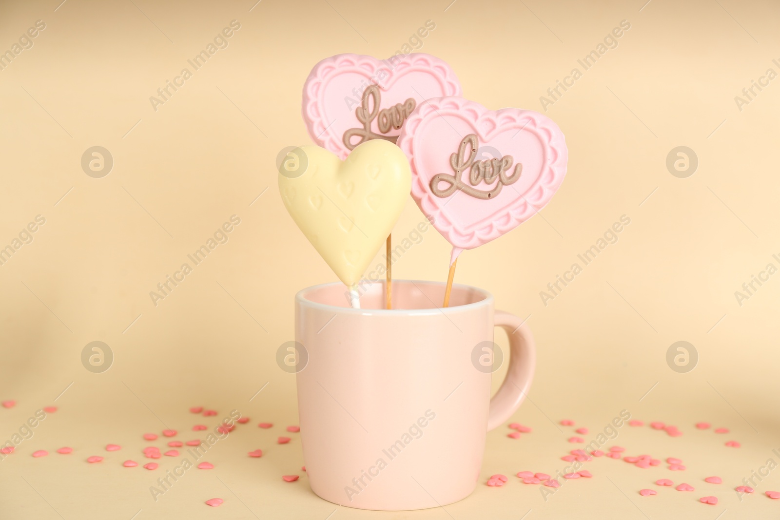 Photo of Different chocolate heart shaped lollipops in cup on beige background