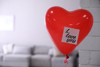 Photo of Red heart shaped air balloon with sticky note saying I Love You in room. Space for text