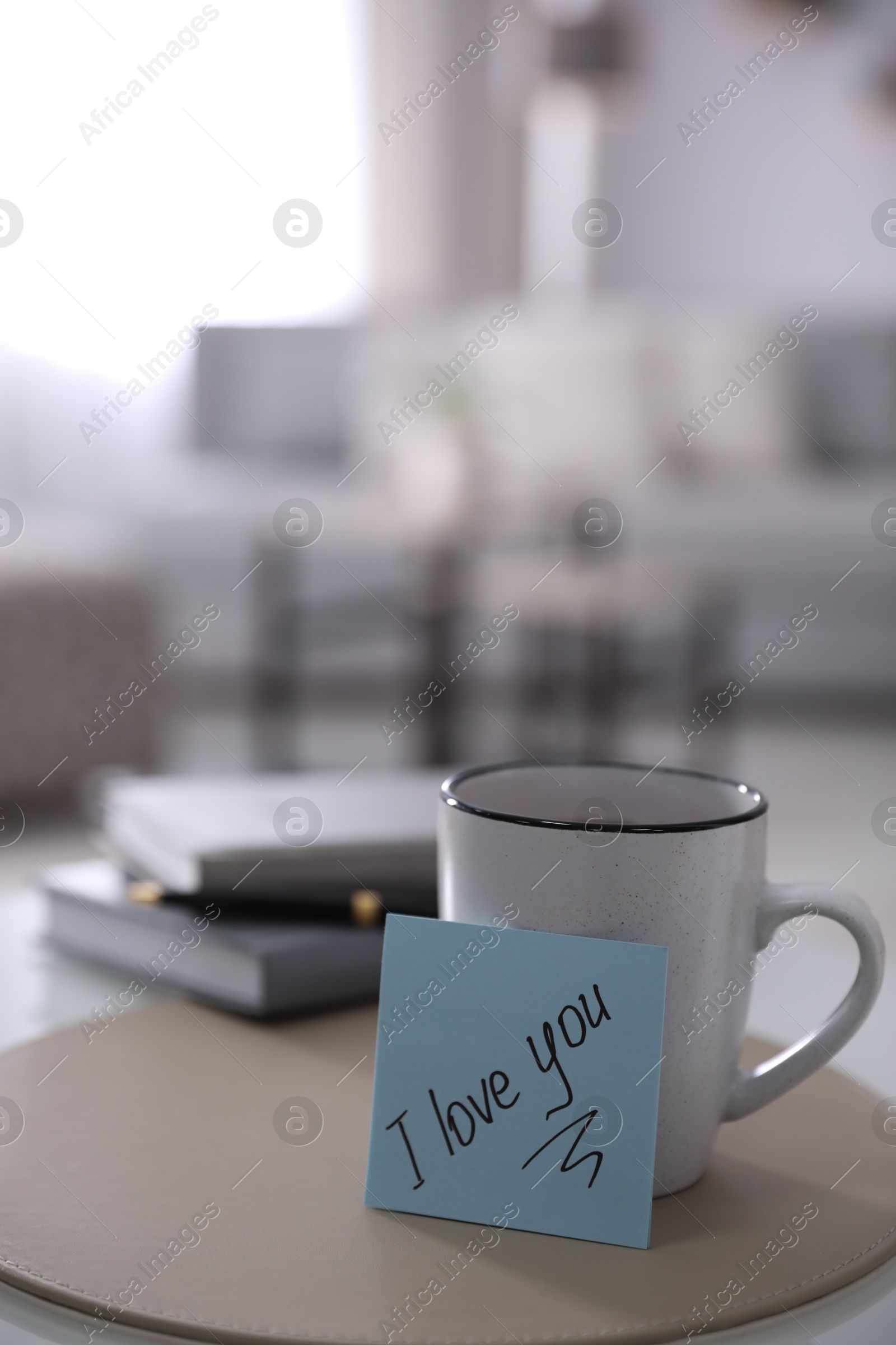 Photo of Paper note with handwritten words I Love You and cup on table indoors. Space for text