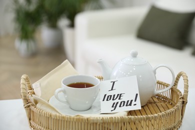 Photo of Paper note with handwritten words I Love You and tea on wicker tray indoors