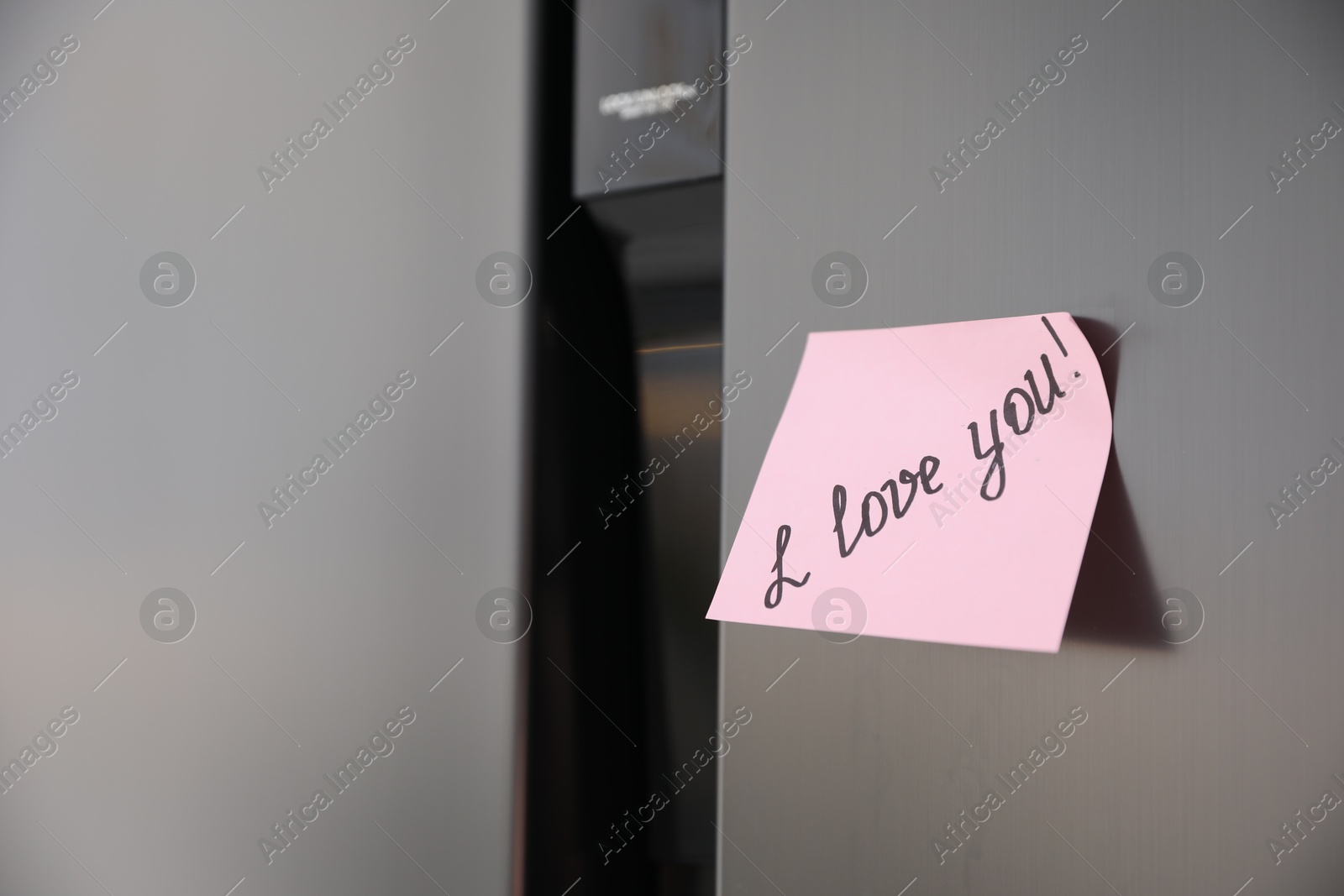 Photo of Sticky note with handwritten text I Love You attached to fridge door. Romantic message