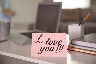 Photo of Note with handwritten text I Love You on workplace. Romantic message