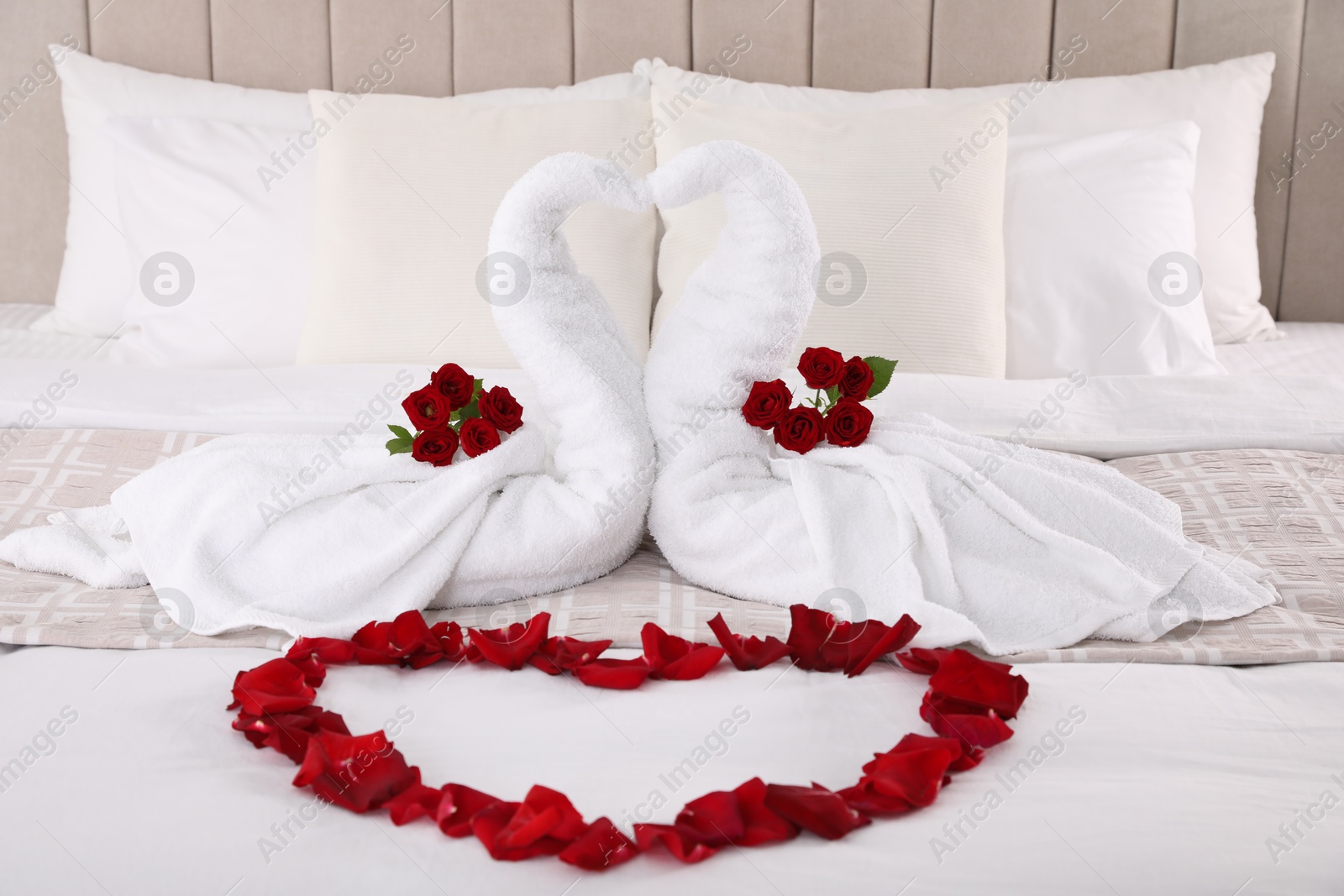 Photo of Beautiful composition on bed. Swans made of towels and rose petals arranged in heart shape