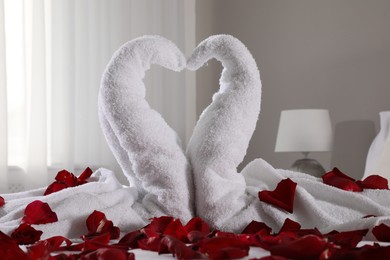 Photo of Beautiful swans made of towels and red rose petals on bed in room