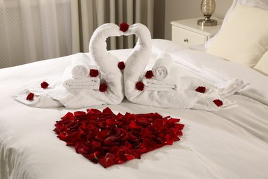 Photo of Beautiful composition on bed. Swans made of towels and rose petals arranged in heart shape