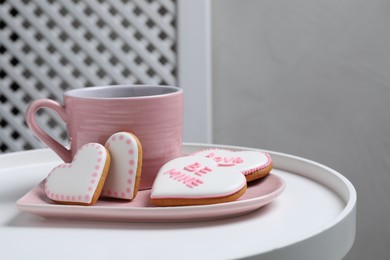 Photo of Delicious heart shaped cookies and cup of hot drink on white table